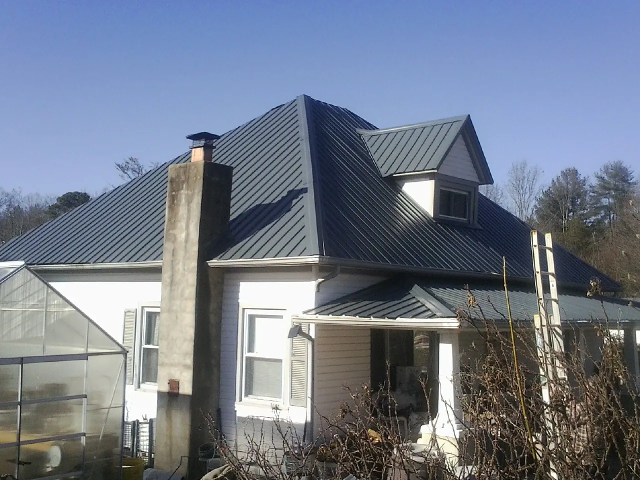 Dark blue standing seam metal roof on a white farmhouse with dormer — Slate & Tile Roof Repair by Roofing Brothers in Winter Springs
