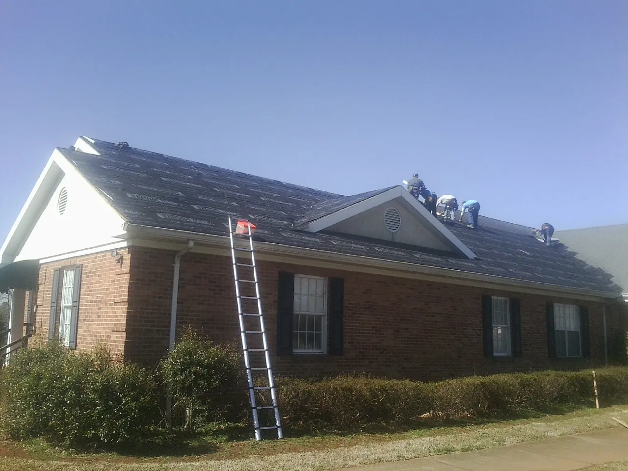 Crew tearing shingles off a brick ranch roof with a ladder set — Metal Roof Repair work by our crew in Winter Springs