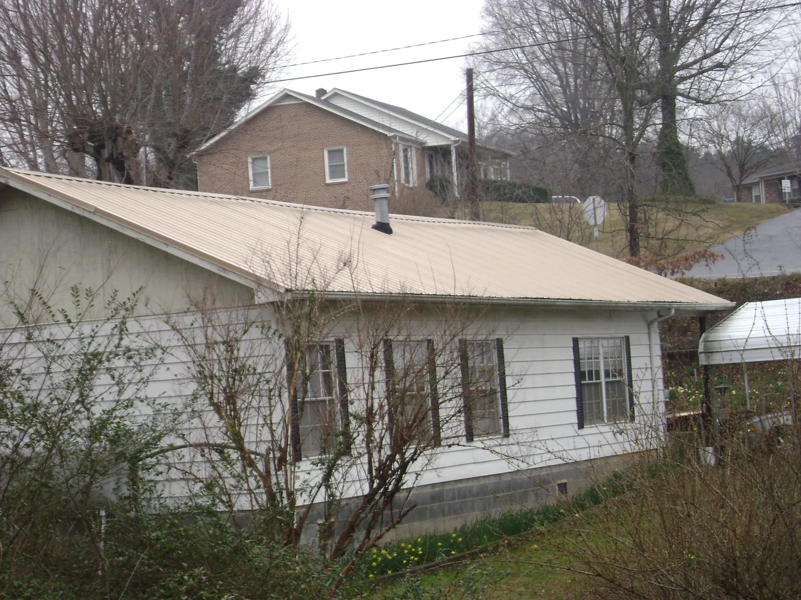 Tan metal roof on a white sided house set into a hillside — Commercial Roofing by Roofing Brothers in Winter Springs
